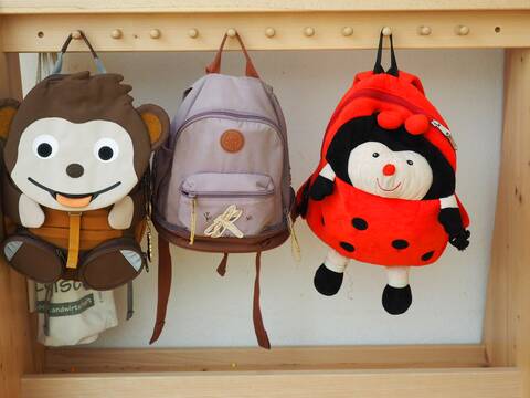 An einer Garderobe im Kindergarten hängen drei Rucksäcke: ein Affe, ein normaler Rucksack und ein Marienkäfer.