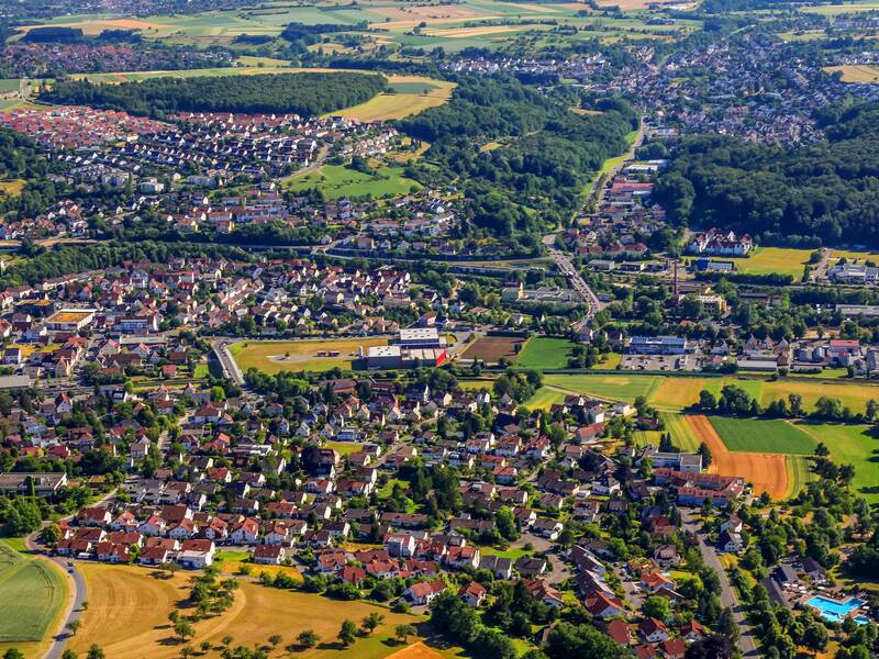 Die Stadt Uhingen von der Luft aus gesehen. Am Boden befinden sich zahlreiche Gebäude und Straßen. Auch die umliegenden Felder und Wälder sind zu sehen.