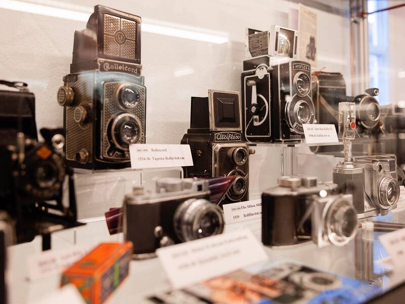 In einer Vitrine sind mehrere Fotoapparate zu sehen, die die Entwicklung der analogen Fotografie nachempfinden sollen. 