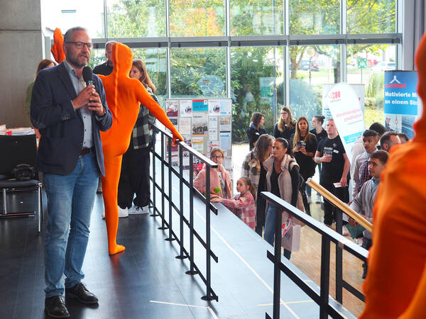 Uhingens Bürgermeister Matthias Wittlinger steht auf der Bühne im Uditorium und spricht in ein Mikrofon. Vor ihm schauen Zuschauer in seine Richtung. Auf der Bühne stehen auch noch Akrobatinnen des TV Uhingen in orangenen Ganzkörperkostümen.