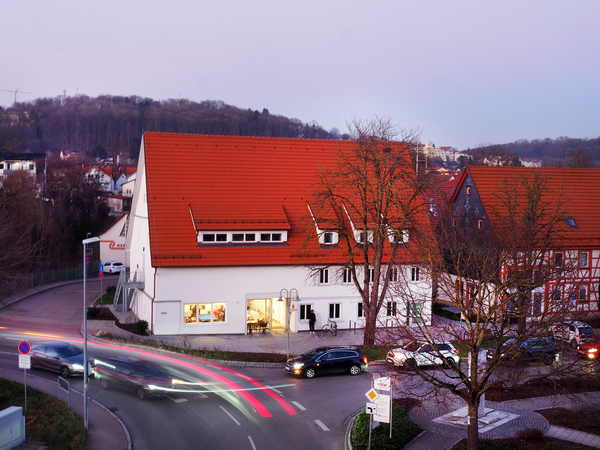 Das K1 in der Abenddämmerung aus erhöhter Perspektive betrachtet. Im Erdgeschoss brennt Licht und vorbeifahrende Fahrzeuge haben ihre Scheinwerfer angschaltet.