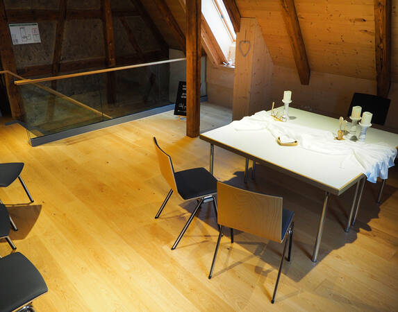 Im obersten Dachgeschoss des K1 steht ein Tisch mit einem Stuhl auf der einen und zwei Stühlen auf der anderen Seite. Der Tisch ist mit einem Tuch und Kerzen für eine standesamtliche Trauung dekoriert.