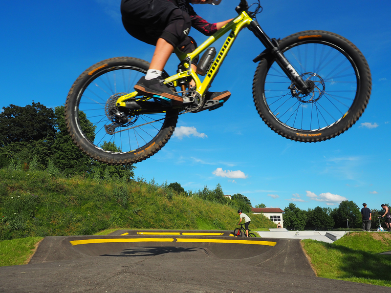 Vor dem blauen Himmel fliegt ein Fahrrad über eine Rampe des Uhinger Pumptracks, einem Parcours für Fahrradfahrer und andere Fahrzeuge.