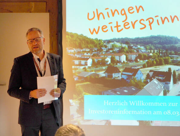 Uhingens Bürgermeister Matthias Wittlinger steht vor einer Präsentation, die eine Grafik für das Spinnweberei-Areal zeigt. Auf dem Entwurf steht der Schriftzug "Uhingen weiterspinnen!"