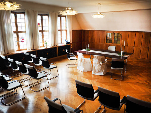 Das Trauzimmer im Rathaus: Im Vordergrund Stuhlreihen und im Hintergrund der dekorierte Trau-Tisch samt Stühlen für das Brautpaar und den Standesbeamten.