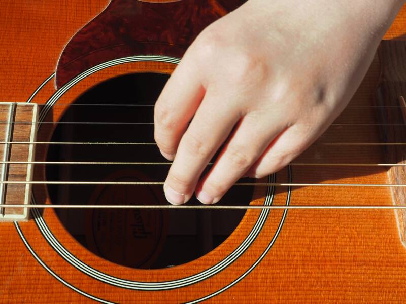 Eine Kinderhand zupft an den Saiten einer Gitarre, Marke Gypsy. Die Gitarre ist braun.