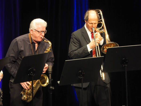 Zwei Herren die hinter Notenständern stehen spielen Saxophon und Posaune.