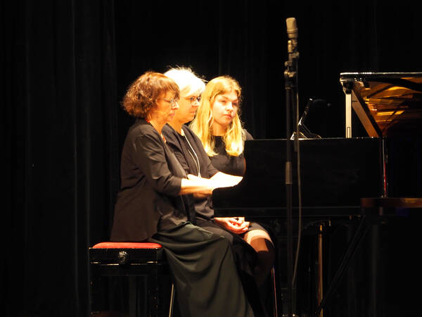 Drei Frauen sitzen nebeneinander auf einer Klavierbank am Flügel und spielen gemeinsam.