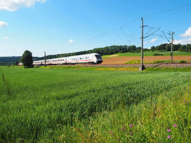 Ein Zug fährt an einem grünen Feld vorbei, der Himmel strahlt blau.