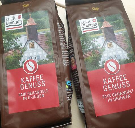 Zwei Kaffeepäckchen mit der Aufschrift Uhinger Kaffeegenuss, fair gehandelt in Uhingen. Auf dem Schmucketikett ist der Giebel und der Turm des Uhinger Rathauses zu sehen.  In der linken Ecke befindet sich das Logo der Stadt Uhingen. 