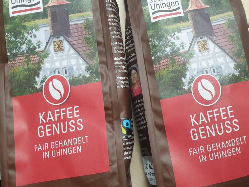 Zwei Kaffeepäckchen mit der Aufschrift Uhinger Kaffeegenuss, fair gehandelt in Uhingen. Auf dem Schmucketikett ist der Giebel und der Turm des Uhinger Rathauses zu sehen.  In der linken Ecke befindet sich das Logo der Stadt Uhingen. 