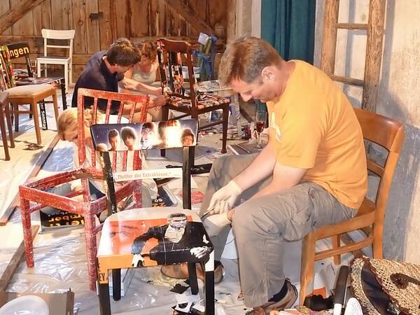 In einer Scheune arbeiten zwei Männer und zwei Frauen  an alten Stühlen. In künstlerischem Ambiente schleifen sie das Holz ab, streichen die Stühle neu oder bekleben sie mit Fotomotiven von Zeitungen und Plakaten. Die Stühle sehen sehr dekorativ aus. 