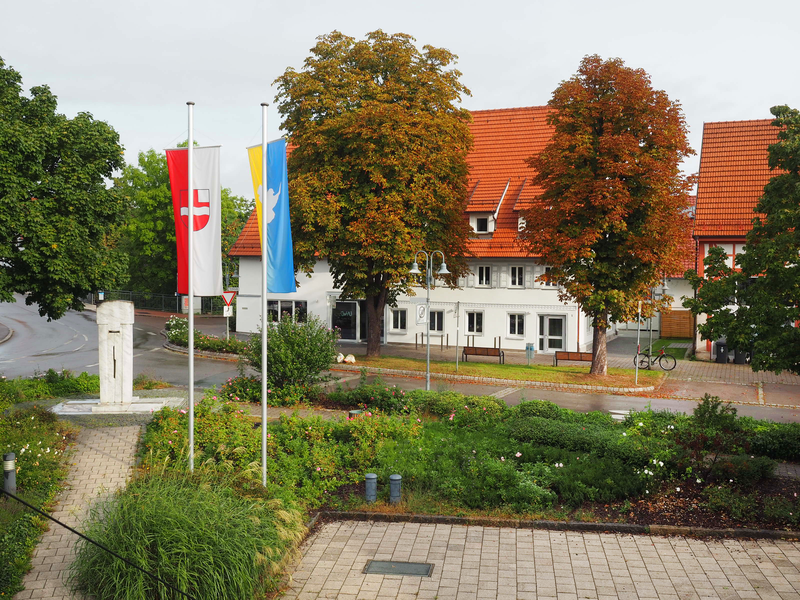 Fahnen wehen vor dem Jugend- und Bürgerhaus K1. Davor befinden sich zwei dichte und große Kastanienbäume.