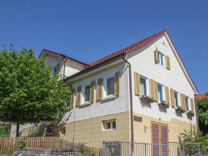 Das Rathaus von Baiereck mit einem großen Baum im Vordergrund und Blumenkästen an den Fenstern im Obergeschoss.