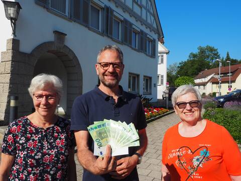 Bürgermeister Matthias Wittlinger mit einem Bündel Geldscheine in der Hand vor dem Rathaus. Neben ihm stehen Doris Oster und Margarete Wais, die vom  Café Fair eine Spende überreicht haben.