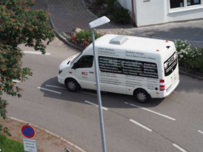 Ein weißer Kleinbus, der Uli-Bürgerbus der Uhinger Linie, fährt auf einer Straße.