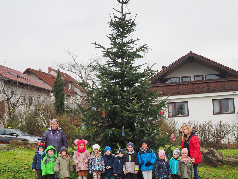 Mädchen und Jungen des Kindergartens im Uhinger Stadtteil Diegelsberg stehen mit zwei Erwachsenen vor dem geschmückten Weihnachtsbaum im Freien.