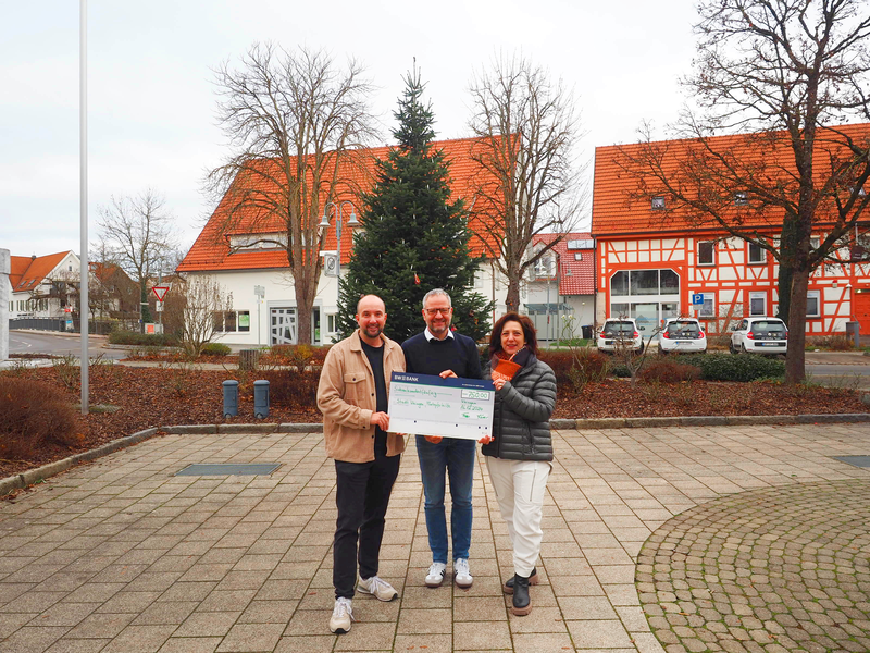 Zwei Männer und eine Frau stehen im Freien vor einem geschmückten Weihnachtsbaum und präsentieren einen großen Scheck. Simon Frey (links) und Sylvia Kneer überreichen den Spendenscheck an Matthias Wittlinger zugunsten der Bürgerstiftung der Stadt Uhingen.