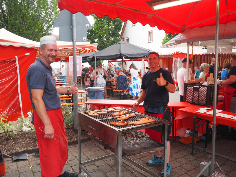 Zwei Männer stehen an einem Grill und heben einen Daumen hoch