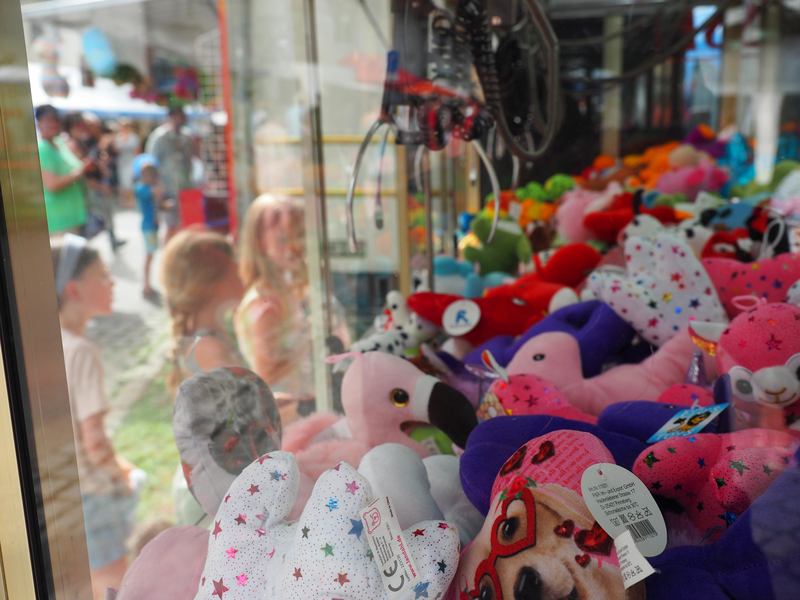 Kinder stehen vor einem Glaskasten, aus dem sie mit Greifarm Kuscheltiere greifen können.