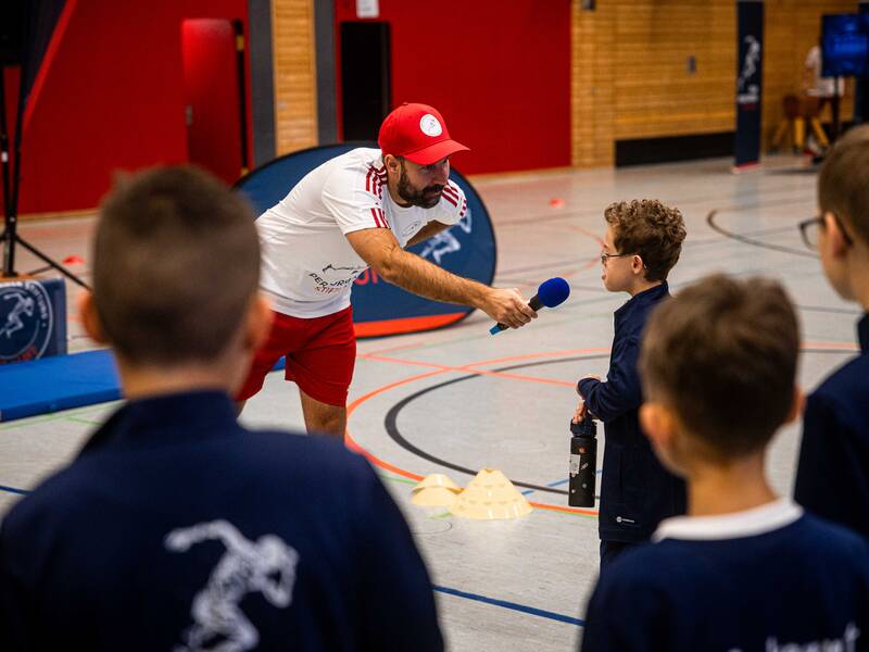 Ein Sportler hält in einer Turnhalle einem Jungen ein Mikrofon vors Gesicht.