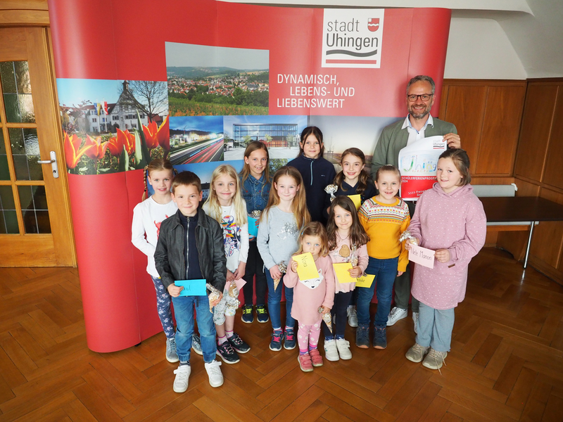 Mehrere Kinder stehen mit Bürgermeister Matthias Wittlinger vor einer roten Stellwand und lachen in die Kamera.