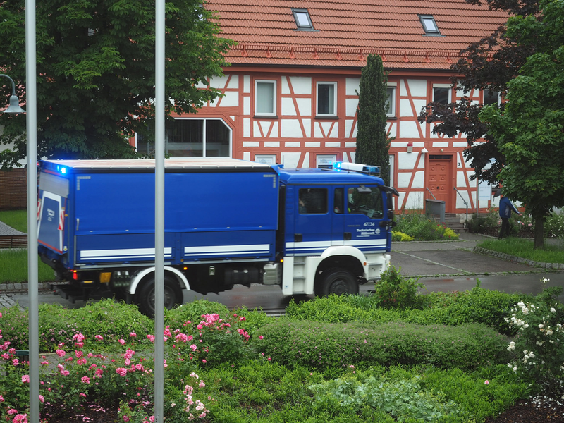 Ein blau-weißer Lastwagen des Technischen Hilfswerks steht auf einer Straße vor einem Fachwerkbau.