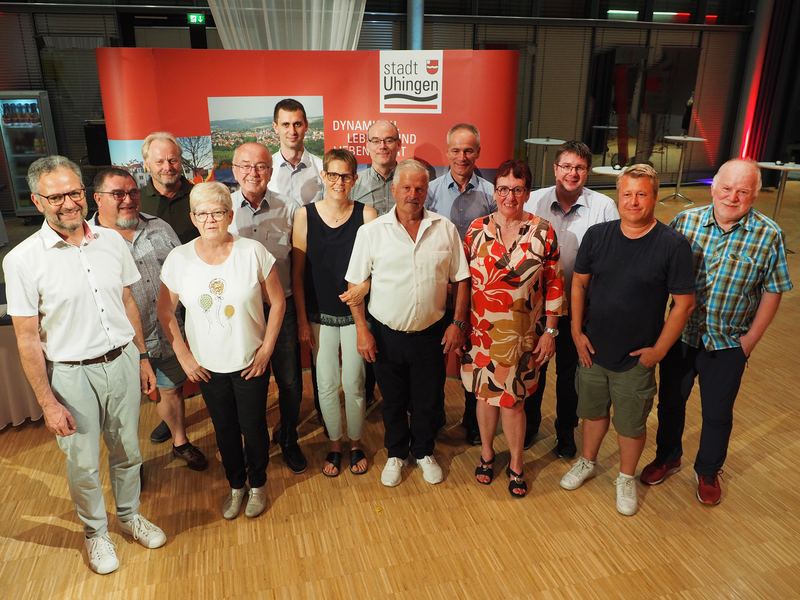 Matthias Wittlinger steht mit Gemeinderätinnen und Gemeinderäten vor einer roten Messewand. Er verabschiedete und ehrte die Mandatsträger.