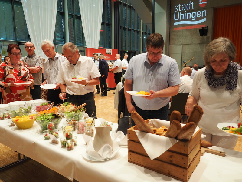 Mehrere Frauen und Männer stehen an einem Buffet und laden sich Essen auf die Teller.