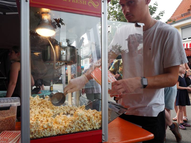 Ein Mann holt aus einem Popcorn-Automaten Popcorn und befüllt eine Papiertüte damit.