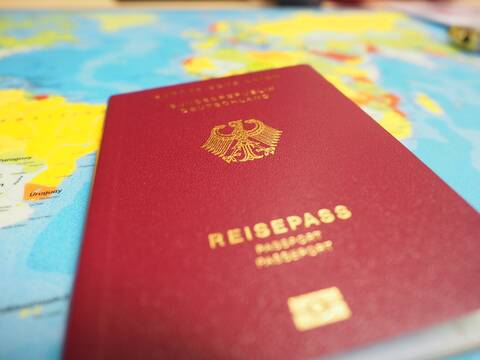 Ein Reisepass mit rotem Einband vor einer Weltkarte.