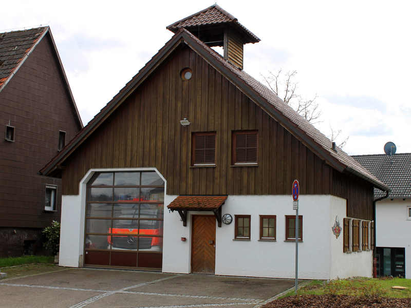 Das Gebäude der Feuerwehr im Stadtteil Diegelsberg mit weißer Fassade und Holzvertäfelung sowie einem kleinen Turm. Hinter dem geschlossenen Rolltor steht ein Einsatzwagen.