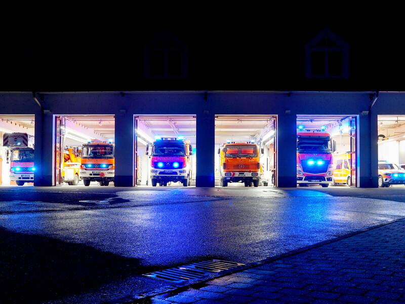 Mehrere Einsatzfahrzeuge der Feuerwehr Uhingen stehen in der Nacht in der beleuchteten Fahrzeughalle mit Blaulicht.