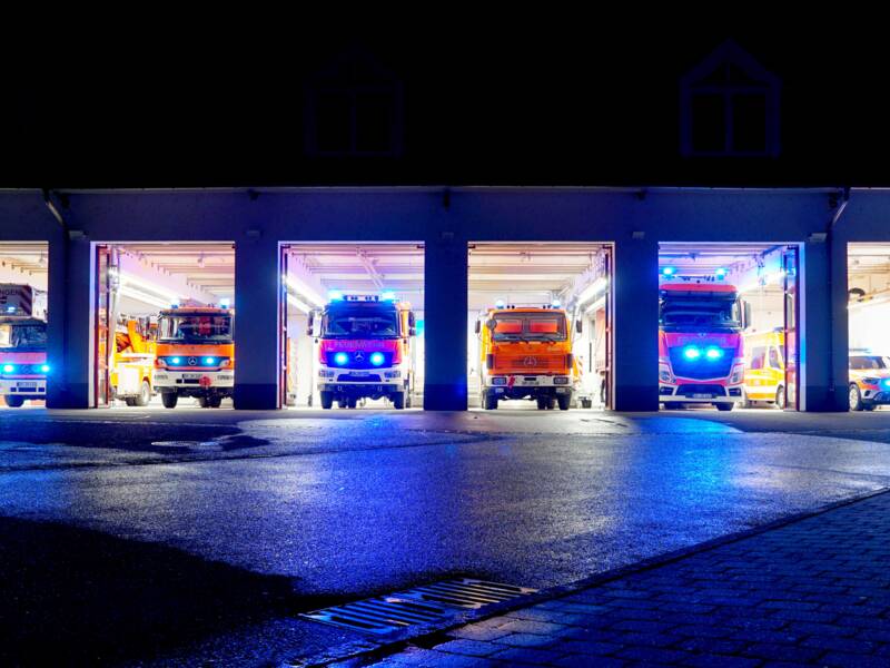 Mehrere Einsatzfahrzeuge der Feuerwehr Uhingen stehen in der Nacht in der beleuchteten Fahrzeughalle mit Blaulicht.