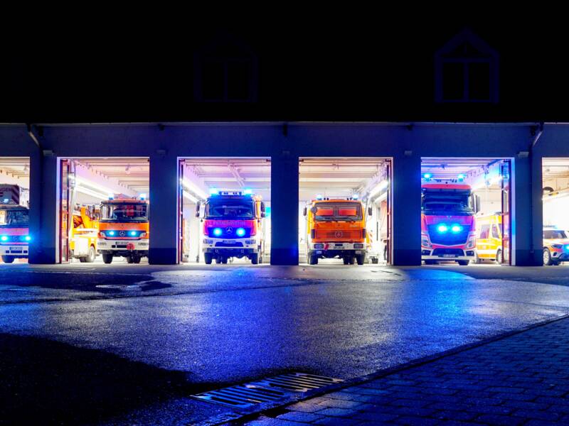 Mehrere Einsatzfahrzeuge der Feuerwehr Uhingen stehen in der Nacht in der beleuchteten Fahrzeughalle mit Blaulicht.